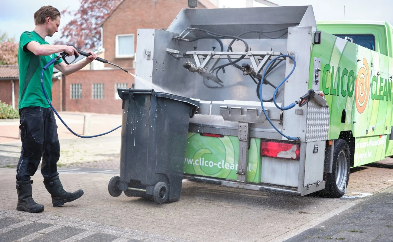 Adriaan en Henry van Clico Clean reinigt een afvalcontainer met hoge druk naast de reinigingswagen